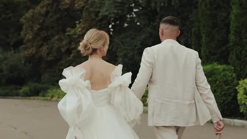 Rear View Romantic Wedding Couple in Elegant Attire Walking Holding Hands