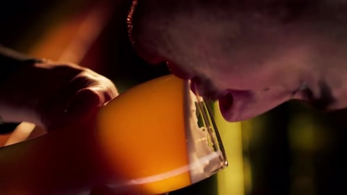 Vertikale Video-Nahaufnahme auf einem hölzernen Bartisch, Typ trinkt aus einem Glas mit hellem Bier, warmer Beleuchtung