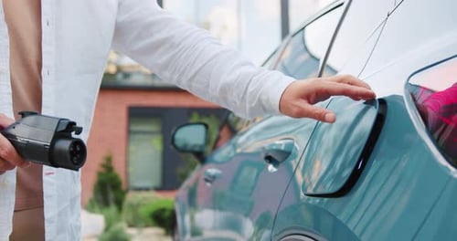 Nahaufnahme männlicher Hände, die ein Elektroauto-Ladegerät mit einem entladenen Fahrzeug verbinden und das Ladegerät starten