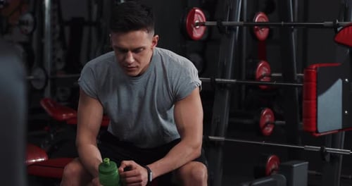 Portrait Attractive Man Drinking Water While Resting in the Gym Look at Camera Use Smart Watch