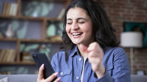 Excited woman celebrates success while using smartphone