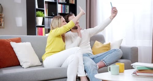 Happy Couple Taking Selfie on Sofa Together Indoors