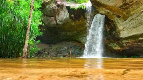 Waterfall Cascades Through Rock Archway Into Pool