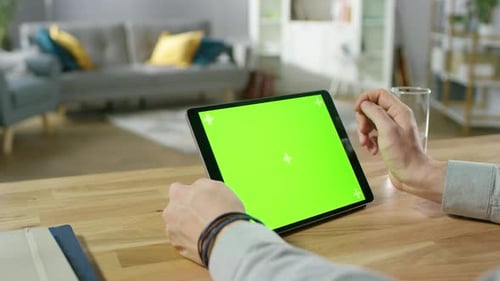 Mann hält und verwendet Handgesten auf einem digitalen Tablet-Computer mit grünem Modellbildschirm, während er sitzt