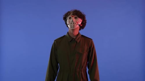 Man in White Mask Looking Around and Showing OK Gesture with Fingers on Blue Background with Red