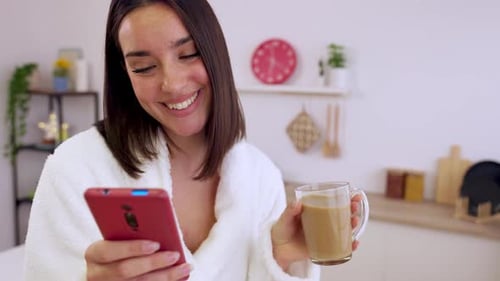 Woman in Robe Using Phone and Holding Drink