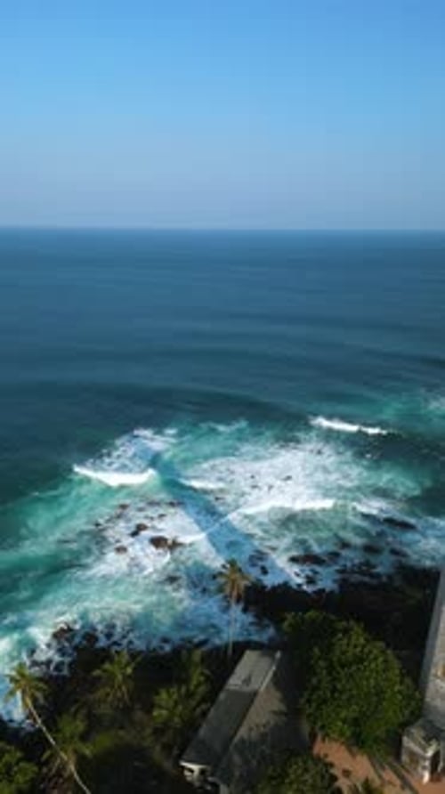 Aerial View Captures Waves Crashing Against Tropical Coastline with Historic Lighthouse Surrounded