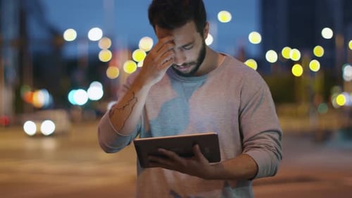Attractive Man using Tablet Computer on Streets of Night Town.