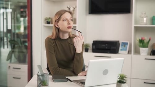 The young woman is sitting at a table in a modern, bright office. She is tired, disappointed, and ex