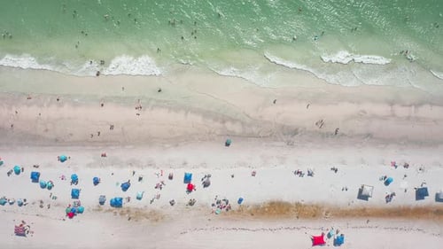 Top-down view of beachgoers and umbrellas along turquoise shoreline