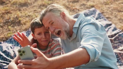 Grandfather and Grandson Video Chat Outside on Sunny Day