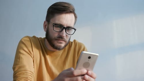 Man with glasses looks at smartphone in home