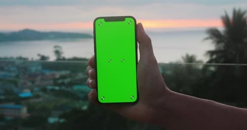 Holding Mobile Phone with Green Screen Chroma Key Over Sunset at Sea at Tropical Scenery Male Hand