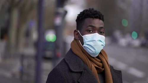 Black African man wearing covid-19 face mask standing outside in street looking at camera