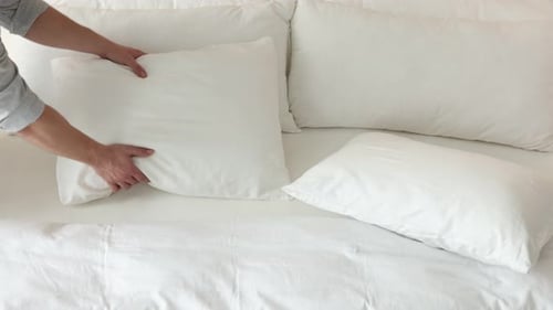 Hands Fluffing White Pillows on Bed in Bedroom