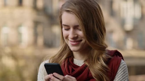 Smiling woman using phone in urban autumn environment