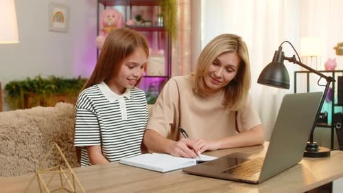 Child Girl Kid with Mother Studying at Home on Sofa and Making Homework Notes in School Notebook