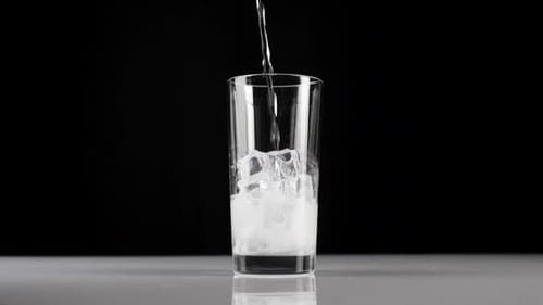 Pure fresh mineral water is poured into a transparent glass with ice cubes on a black background