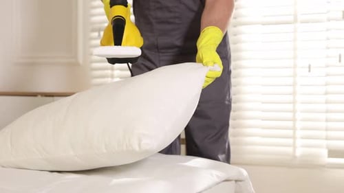 Man Steaming Pillow in Bedroom with Steamer