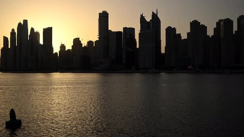 A City Skyline with Tall Buildings Stands in the Background While a Large Body of Water Glistens in