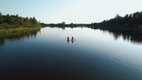 Two Young Women Surf Down River on Surfboards Steering Paddle From Bird's Eye View Steep Bank with