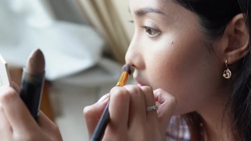 Close up portrait of beautiful young Asian woman applying make up using make up brush and puff