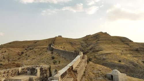 Ancient Hilltop Fortress Wall with Watchtowers and Staircase in Arid Landscape