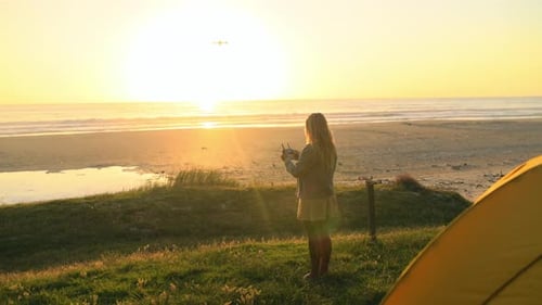 Woman pilot drone at beach, sunset and quadcopter flight in air, spy or surveillance at camping