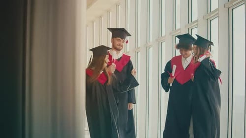 Positive Graduates Dancing With Diplomas in Hallway of a University Building