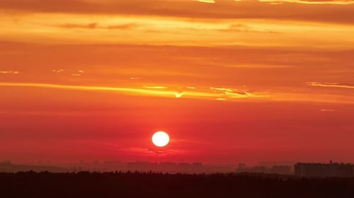 A big red sun in the sunset sky over the roofs of buildings, urban landscape