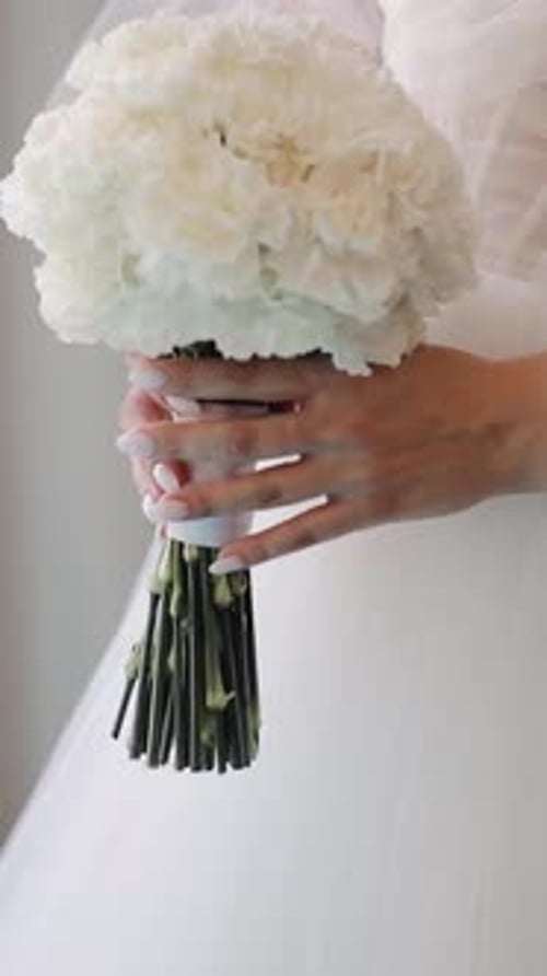 Close up of a bride holding flowers in bedroom. Charming woman holds wedding bouquet of flowers indo