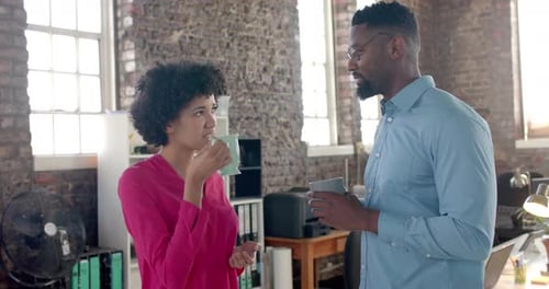 Happy diverse colleagues discussing work and drinking coffee in office in slow motion