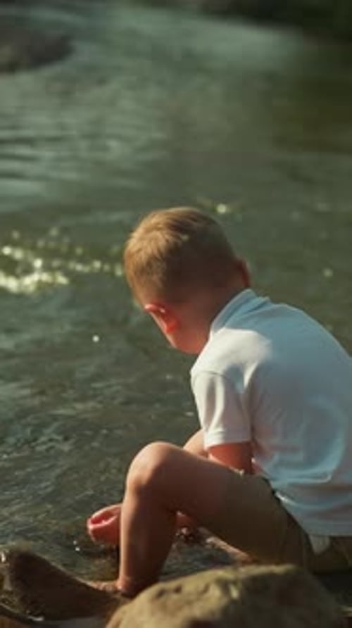 Adorable Toddler Boy Touches Water with Hands on Lake Bank