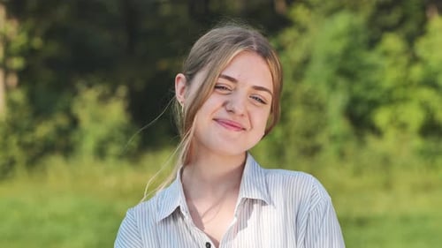 Young Girl Smiling Happily in a Sunny Park Surrounded By Lush Greenery and Tall Trees Radiating