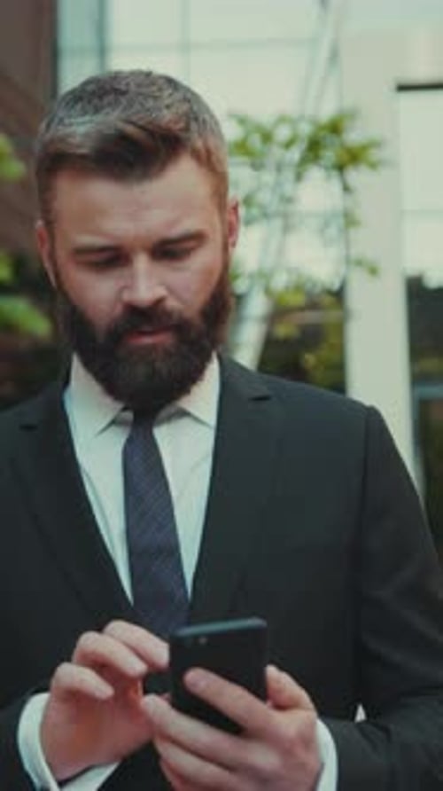 Satisfied Successful Business Man Uses Smartphone While Walking on the Big City Business District
