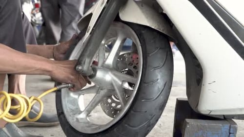 Mechanic pumping air into wheel of motorbike, static close up view