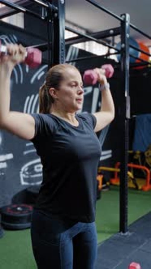 Determined Woman Training Shoulders with Dumbbells at Gym