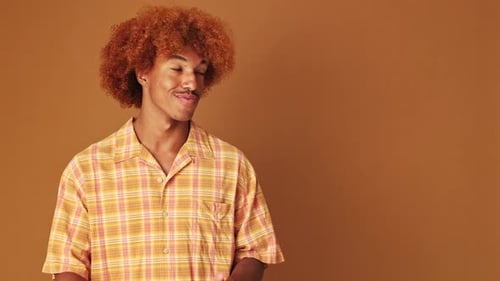 Guy points to the side at pointing fingers to show mockup space, isolated on brown background
