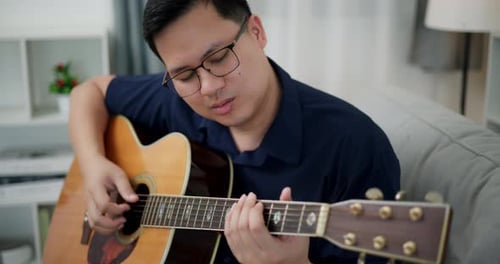 Young Adult Man Playing Acoustic Guitar at Home