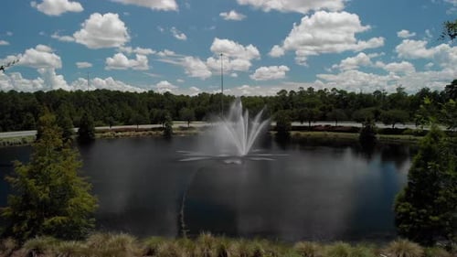 Langsamer Einstoß, vorbei an Bäumen auf der Seite, zum Vorschein kommt ein Springbrunnen im Teich mit Bäumen rund um das Wasser
