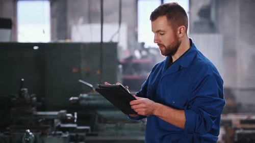 Factory worker is standing in warehouse and typing information in the tablet