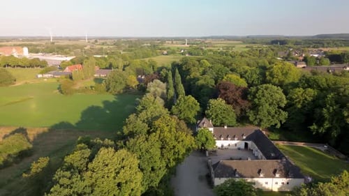 A charming historic estate with a U-shaped courtyard, surrounded by lush greenery, fields, and trees