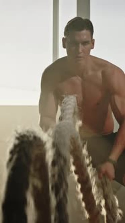 Dedicated Motivated Caucasian Male Athlete Training Shirtless in Gym with Battle Ropes