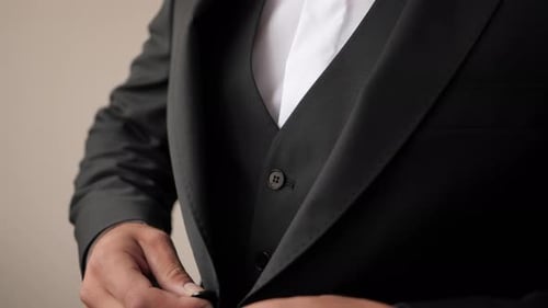 Close-up shot of a groom getting ready and buttoning his black wedding suit wearing wooden bow tie a