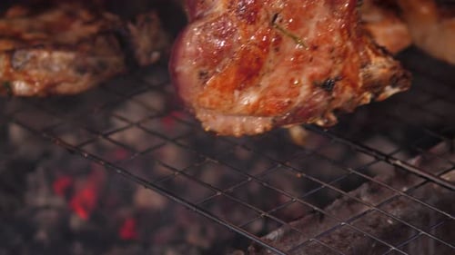 Closeup of a Man Frying Pork Steak Over a Campfire on a Grill in the Evening
