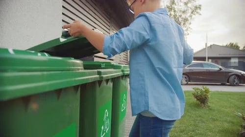 Young Boy is Walking Outside His Home in Order to Throw Away Two Empty Plastic Bottles into a Trash
