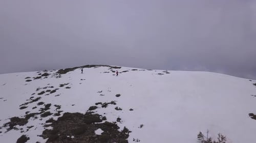 Aerial view from drone of two people walking across snowy mountain ridge with dark gloomy sky backgr