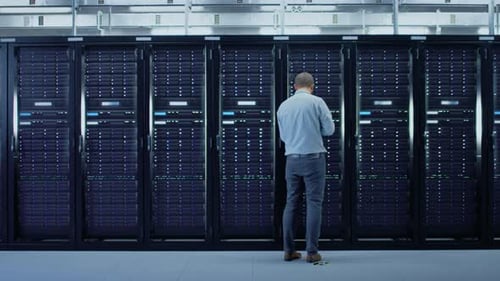 Bearded IT Specialist in Glasses is Working on Laptop in Data Center while Standing Before Server R