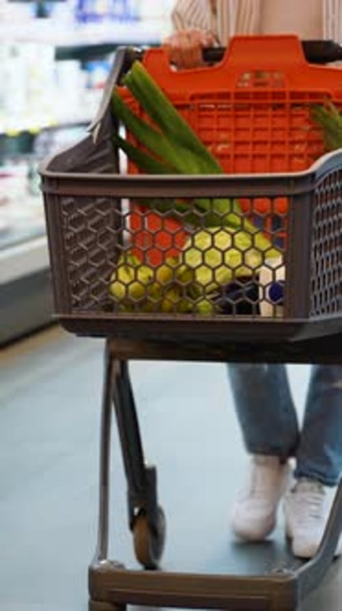 A Woman Shopper Confidently Pushes a Cart Overflowing with Fresh Groceries in Supermarket Vertical