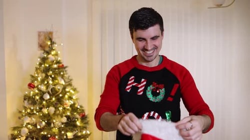 Man Puts on Santa Hat in Front of Christmas Tree